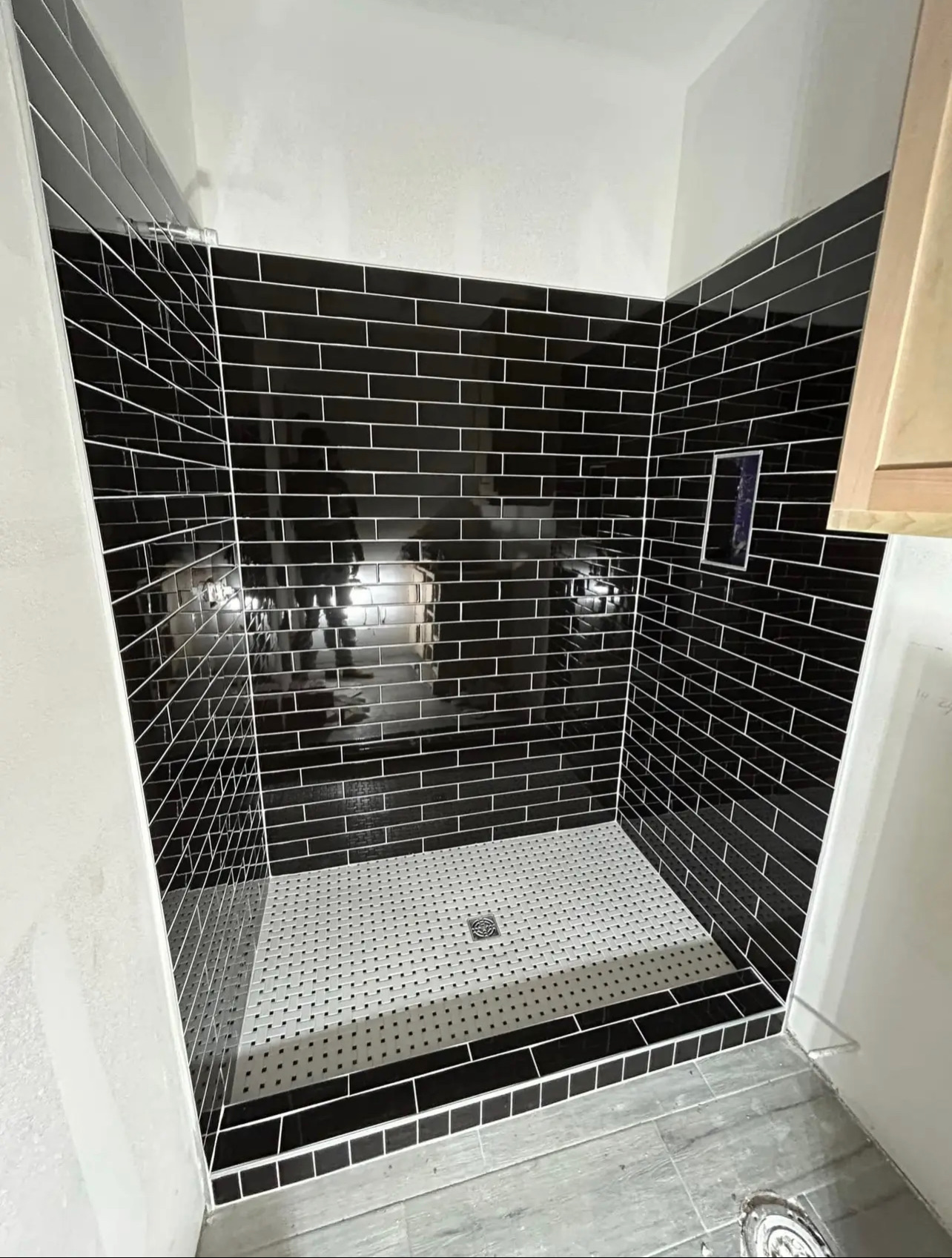 Walk-in shower with glossy black subway tile walls, white grout, niche, and white mosaic floor