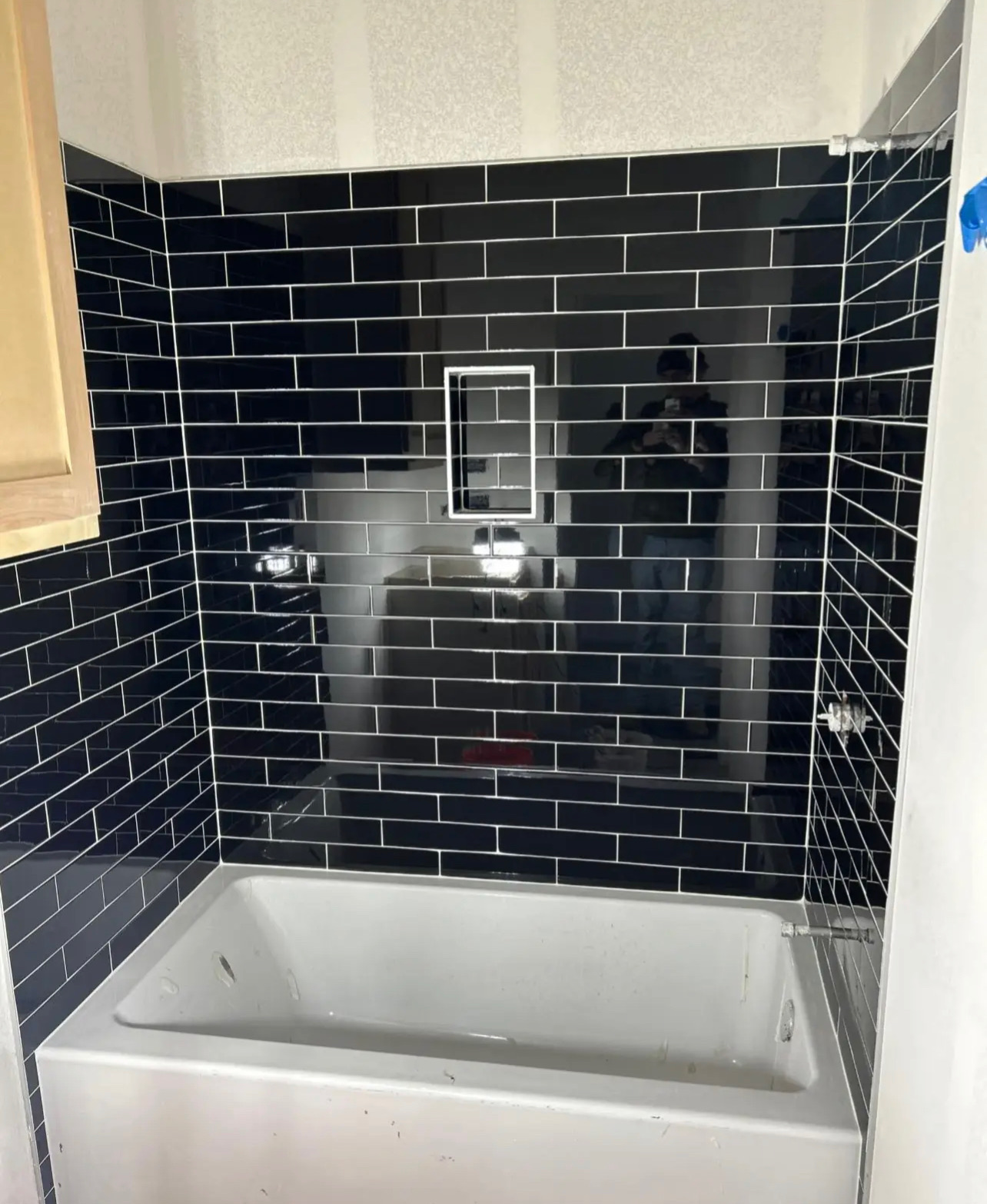 Alcove bathtub surround in glossy black subway tile with white grout and recessed niche