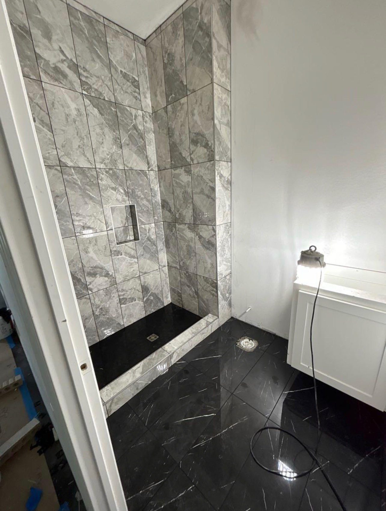 Bathroom with vertical marble-look shower walls and polished black floor tile